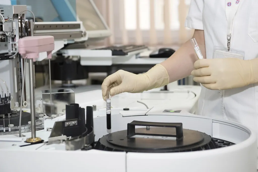 Lab technician in gloves handling a blood sample tube beside a laboratory analyzer