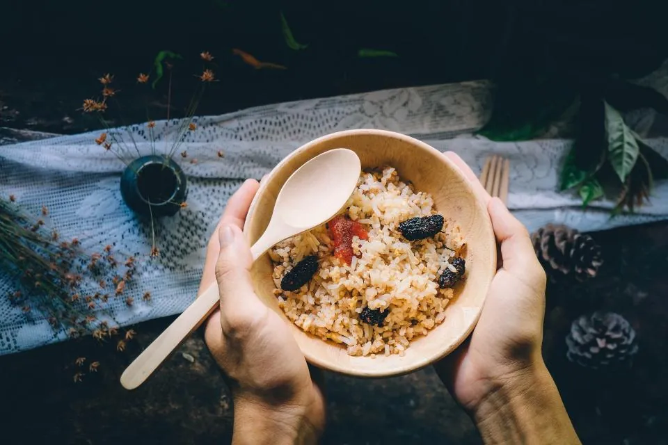 Hands holding a bowl of mixed grains and vegetables with a wooden spoon, a carbohydrate portion to count