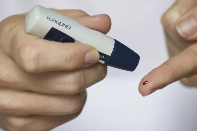Person holding a lancing device next to a fingertip with a small drop of blood for a home blood sugar check