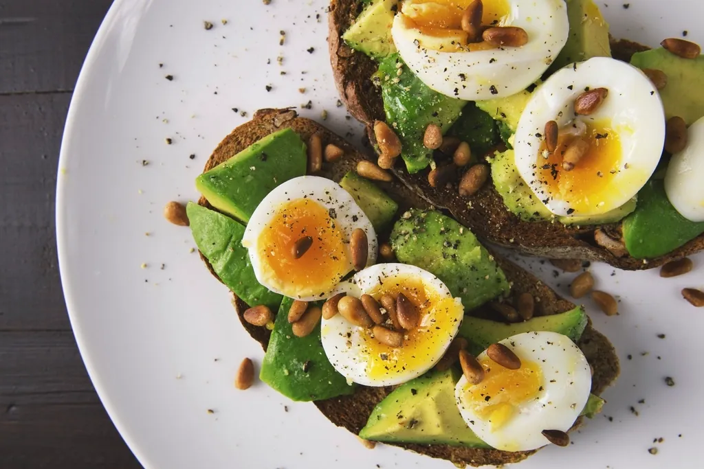 Whole-grain toast topped with avocado, soft-boiled eggs and seeds on a white plate