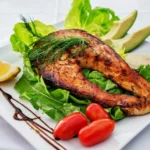 Plate of grilled salmon with leafy greens, tomatoes, avocado and lemon showing a balanced diabetes plate
