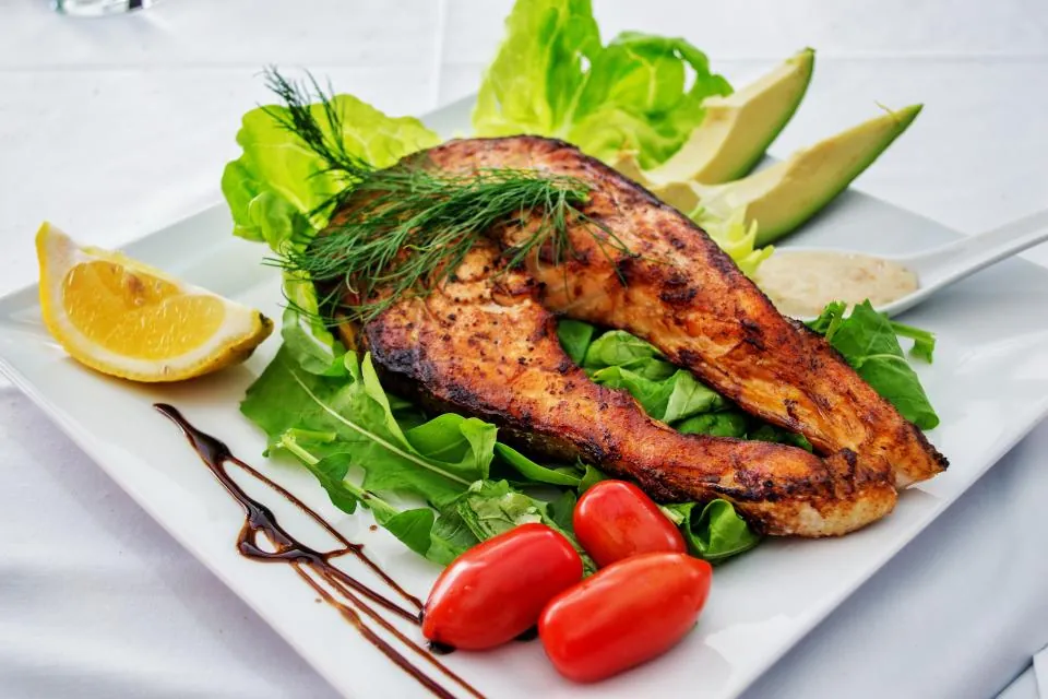 Plate of grilled salmon with leafy greens, tomatoes, avocado and lemon showing a balanced diabetes plate