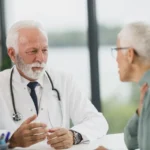 Doctor in a white coat talking with an older patient at a clinic desk