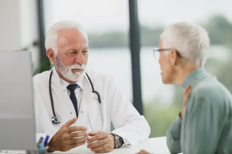 Doctor in a white coat talking with an older patient at a clinic desk