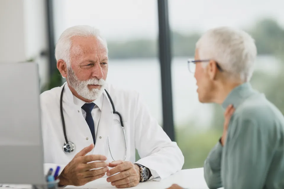 Doctor in a white coat talking with an older patient at a clinic desk