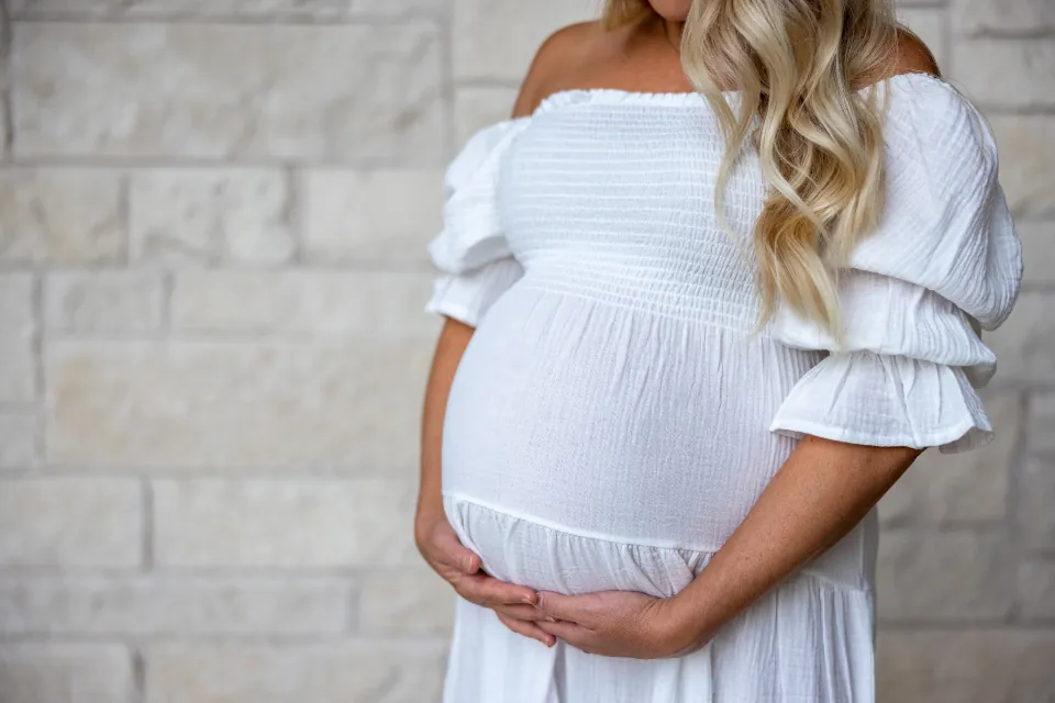 Pregnant woman in a white dress holding her belly