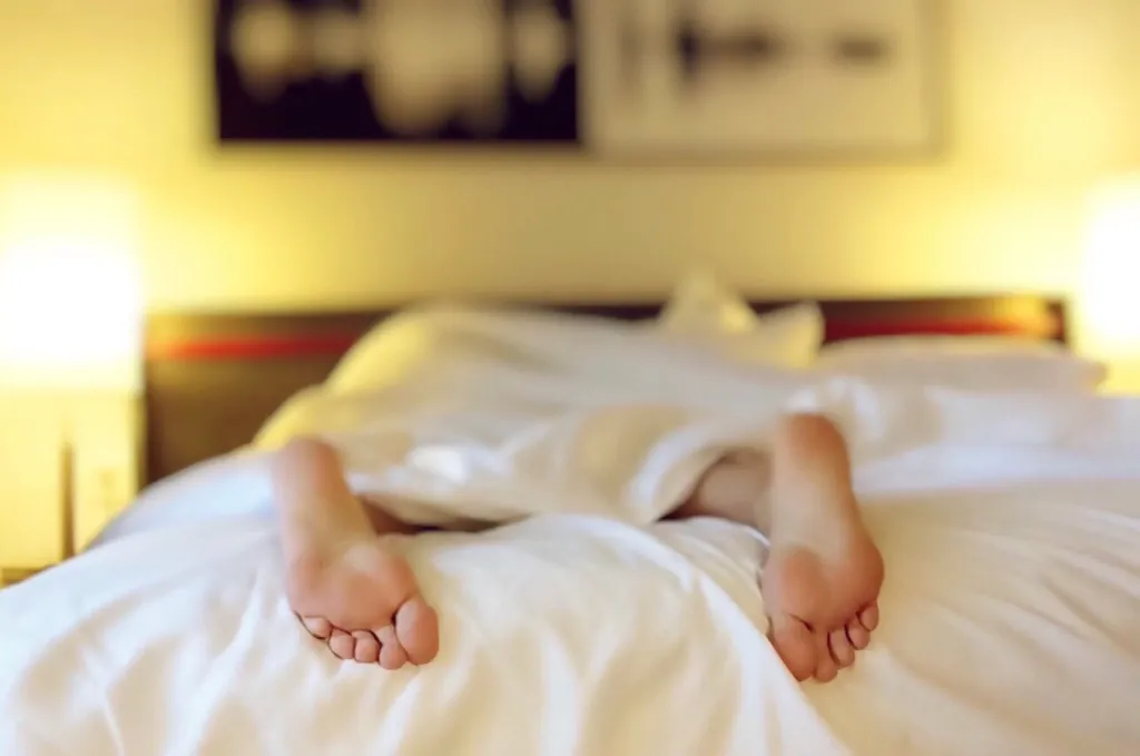 Person resting in a bed with white sheets in a warmly lit bedroom